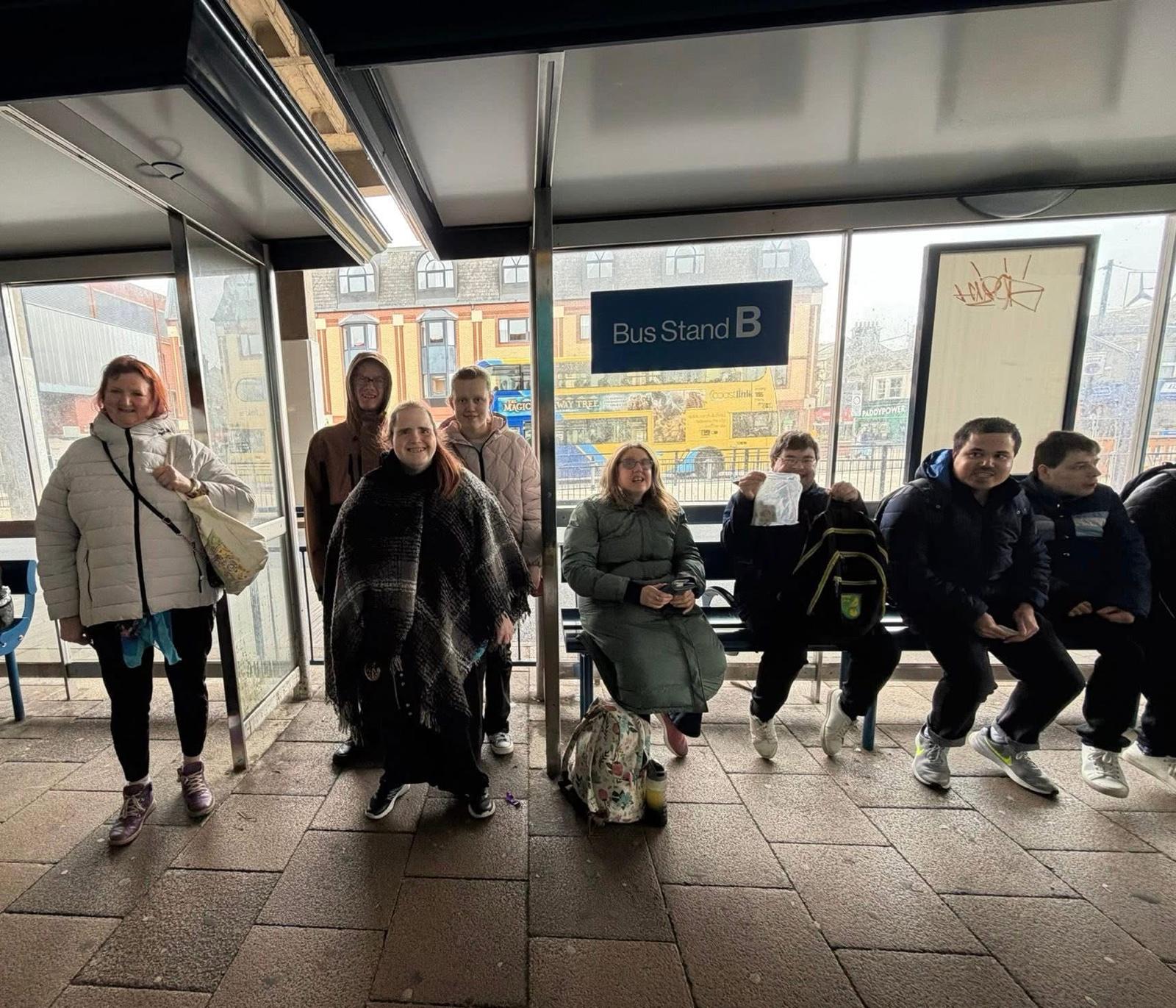 A group from Seabreeze waiting at a bus stand on a community outing